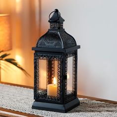 a black lantern with two lit candles sitting on a table