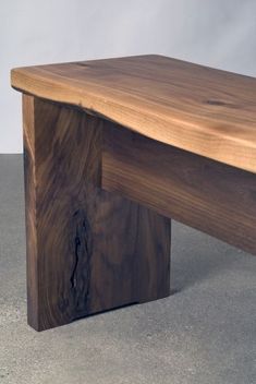 a wooden bench sitting on top of a cement floor next to a white wall in the background