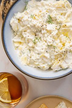 a bowl filled with potato salad next to crackers and lemon wedges