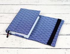 a notebook with a blue cover and black binding is sitting on a white wooden surface