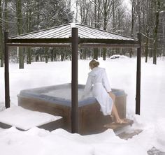 a woman sitting on top of a wooden hot tub in the middle of snow covered ground