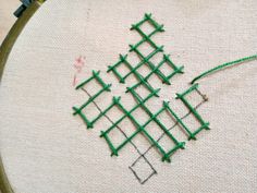 a close up of a cross stitch on a piece of cloth with green thread in the middle