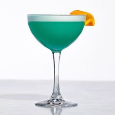 a green cocktail with an orange slice on the rim in a coupe glass against a white background