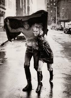 two people are walking in the rain with an umbrella over their heads and boots on