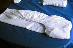 an unmade bed with blue sheets and white pillows