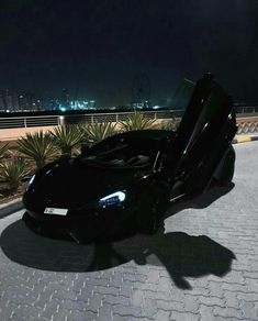 a black sports car parked on the side of a road at night with its door open