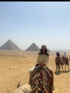 three people riding camels in the desert with pyramids in the backgroud