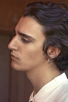 a man with black hair and earrings on his head looking off to the side, wearing a white shirt