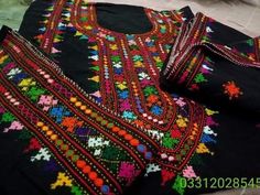 an embroidered black shirt with multicolored flowers and stars on the chest, sitting on top of a bed