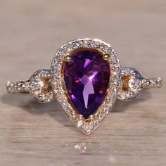 The 14th Avenue: Amethyst Halo Ring With Natural Diamonds In Yellow Gold. The Ring Centers On A 1.50 Carat Pear Brilliant Cut Natural Amethyst With Charming Purple Color. Surrounding The Center Is A Halo Of Round Cut Natural Diamonds. Diamonds Continue Into The Anchor Topped Shank. A Scrolled Filigree Finishes The Look Below The Center. The Ring Is Crafted In 14 Karat Yellow Gold And Is Currently A Finger Size 7 Yet Can Be Adjusted To Any Finger Size For An Additional Charge On Request. Amethyst And Diamond Ring, The Anchor, Halo Ring, Halo Rings, Womens Jewelry Rings, Purple Color, Round Cut, Natural Diamonds, Gold Color