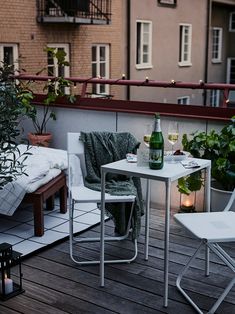 a table and two chairs on a deck next to a building with potted plants