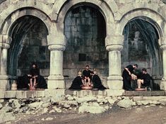 some people are sitting on the ledges in front of an old stone building with arches