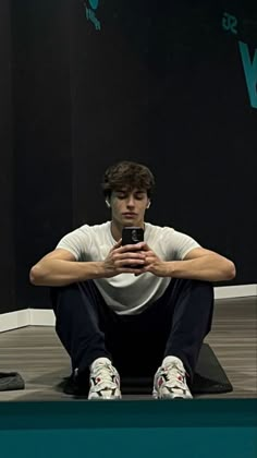 a young man sitting on the floor with his cell phone in hand and looking at it