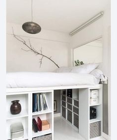 a white bed sitting under a mirror next to a shelf filled with lots of books