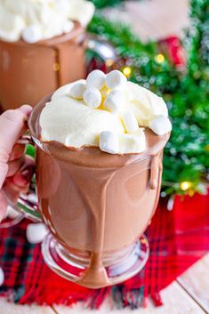 hot chocolate with marshmallows in a mug on a plaid tablecloth next to a christmas tree