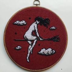 a cross - stitch picture of a woman holding a broom in front of the sky