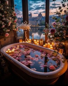 a bathtub filled with candles and flowers next to a window overlooking the city at night