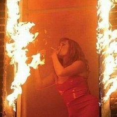 a woman standing in front of a mirror with fire coming out of it's sides