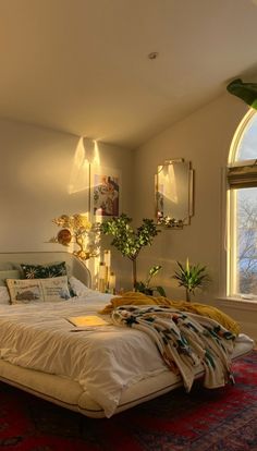 a bedroom with a large bed in front of a window next to a rug and potted plant