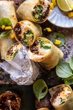 several burritos are wrapped in foil and garnished with fresh herbs, on a table