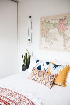 a white bed topped with lots of pillows next to a wall mounted world map on the wall