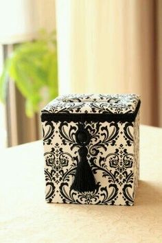 a black and white box with a tassel on it sitting on a table in front of a window