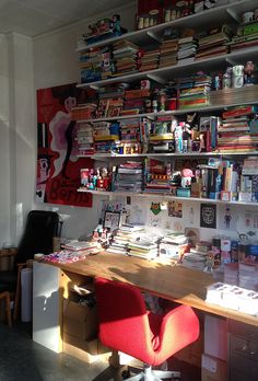 a desk with red chair and bookshelf in the background