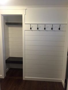 an empty closet with white walls and black hooks on the door, next to a wooden floor