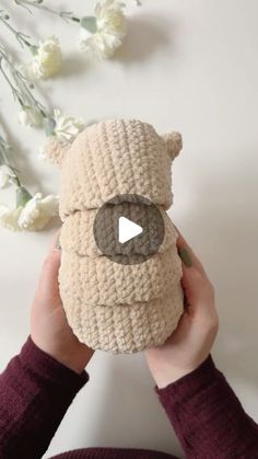 a person holding a crocheted teddy bear in front of a white wall with flowers