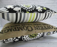 two pillows sitting on top of each other in front of a white brick wall with black and green flowers