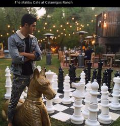 a man standing next to a giant chess set