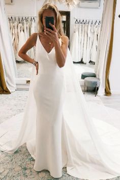 a woman in a white dress taking a selfie with her cell phone while wearing a wedding gown