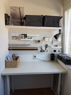 a white desk sitting under a window next to a shelf filled with boxes and other items