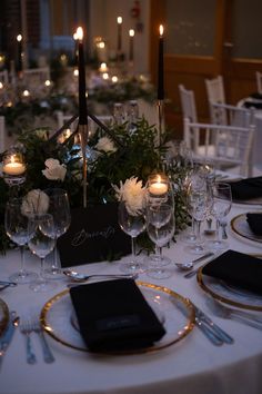 the table is set with white flowers and black napkins, gold rimmed plates and candles