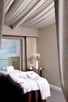 a bed with white sheets and pillows in a room next to a window overlooking the ocean