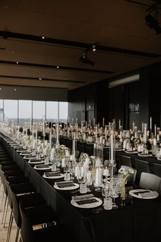 a long table is set up with black linens and white place settings for an event