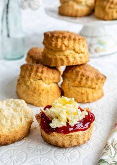 some biscuits and jam are on a white tablecloth next to other muffins