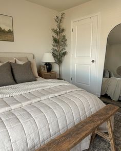 a bedroom with a bed, mirror and wooden bench in front of the door that leads to another room