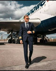 a man in a suit and sunglasses walking towards an airplane on the tarmac at an airport