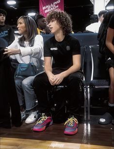 two people sitting on chairs in front of a group of other people at a basketball game