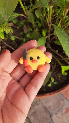 a hand holding a small yellow and black pokemon figurine in front of a potted plant