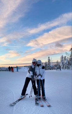 two people on skis standing in the snow with their arms around each other,