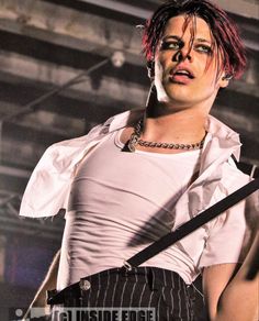 a man with red hair and piercings on his chest holding a guitar in front of him