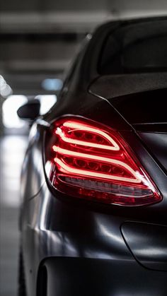 the back end of a black car with its lights on in a parking garage area