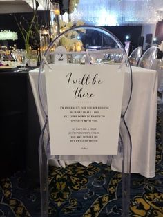 a clear chair with a sign attached to it sitting in front of a table filled with plates and glasses