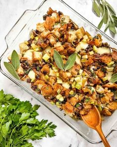 a glass casserole dish filled with stuffing and herbs on top of a marble counter