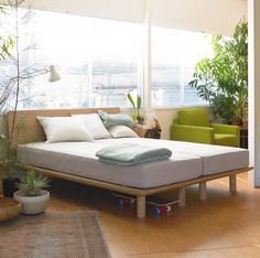 a bed sitting on top of a wooden floor next to a green chair and potted plant