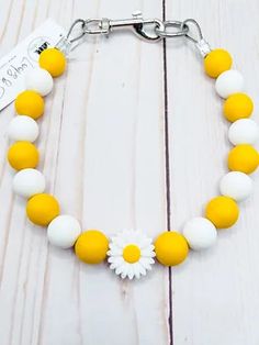 a yellow and white beaded bracelet with a daisy charm on it's side