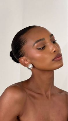 a woman with her eyes closed and wearing large diamond earrings on her left ear, standing against a white wall