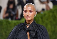 a woman with shaved hair and piercings on her head, wearing a black dress